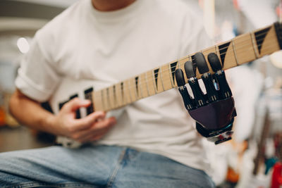 Midsection of man playing guitar with artificial hand