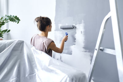 Young woman using paint roller while painting wall at home