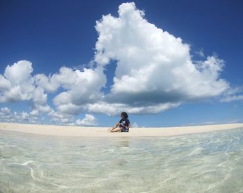 Woman sitting on sand dune in desert against sky