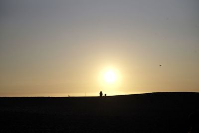 Silhouette people on land against sky during sunset