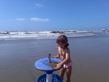 Full length of shirtless boy standing at beach against sky