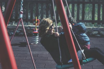 Side view of grandmother with grandson sitting on swing at playground