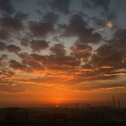 Silhouette buildings against dramatic sky during sunset