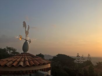 Sculpture on roof of building against sky during sunset