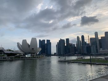 Modern buildings by river against sky in city