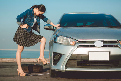 Young woman standing on car against blue sky