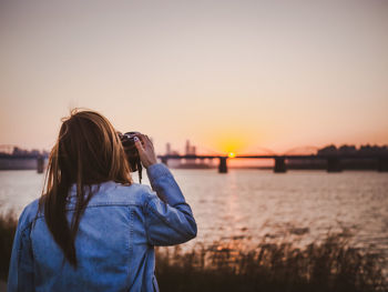 Young woman photographing against sky during sunset