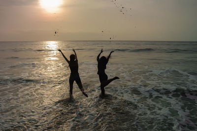 Silhouette people at beach against sky during sunset