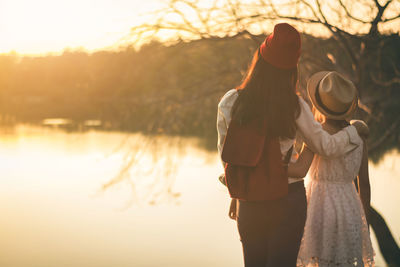 Couple standing by lake against sky during sunset