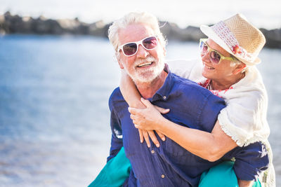 Portrait of cheerful senior man piggybacking woman at beach