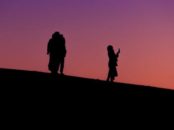 Silhouette people standing against orange sky