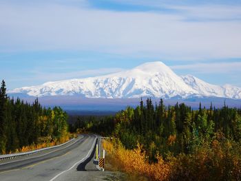 Road amidst trees and snowcapped mountains against sky