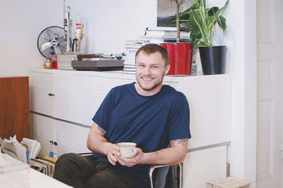 Portrait of happy businessman holding coffee cup while sitting in creative office