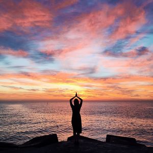 Silhouette woman performing yoga at beach during sunset