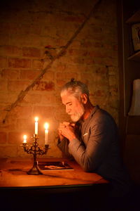 White haired bearded man meditating by candlelight at night