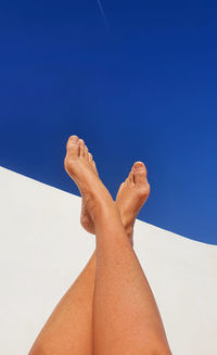 Low section of woman legs against clear blue sky