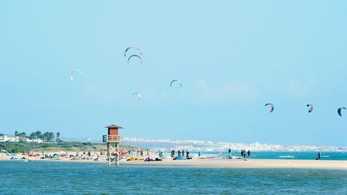 People at beach against parachutes in sky