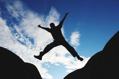 Low angle view of silhouette man with arms raised jumping against sky