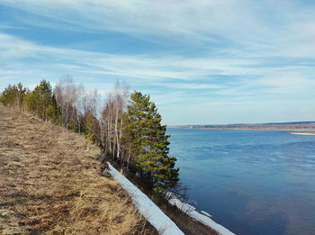 Melting snow on a slope by the river against a blue sky with beautiful clouds on a spring day