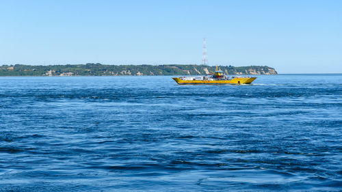 Boat sailing in sea against clear blue sky