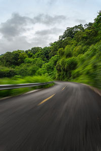 Blurred motion of road amidst trees against sky