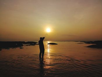 Silhouette person standing in sea against sky during sunset