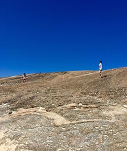 Man walking on landscape against clear blue sky