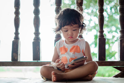 Cute girl watching video over smart phone while sitting against railing