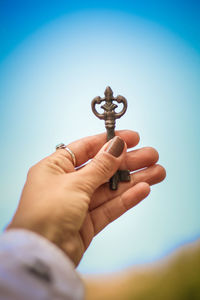 Cropped image of hand holding key against sky