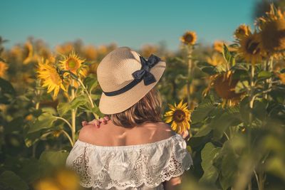 Rear view of woman standing amidst sunflowers on land