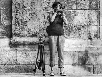 Full length of woman photographing against wall