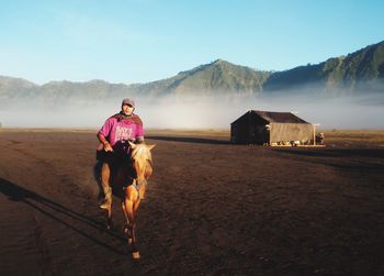 Full length of man riding horse on mountain against sky