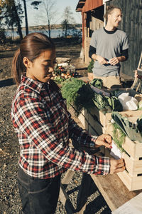 Mature female farmer sticking label on crate full of vegetables at market