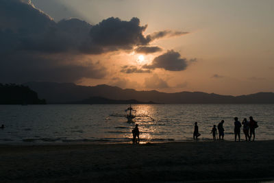 Silhouette people on beach against sky during sunset