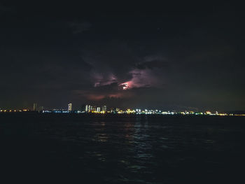 Illuminated city by sea against sky at night