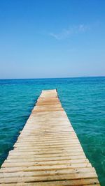 Pier over sea against clear blue sky