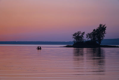 Silhouette people on boat in sea against orange sky