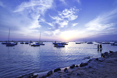 Sailboats moored on sea against sky during sunset