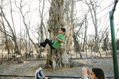 Siblings swinging against bare trees in playground