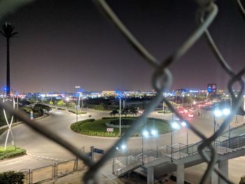 Illuminated cityscape seen through chainlink fence at night