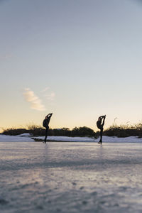 Two female figure skaters practicing together on frozen lake at dusk
