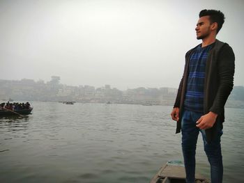 Young man standing by river against sky