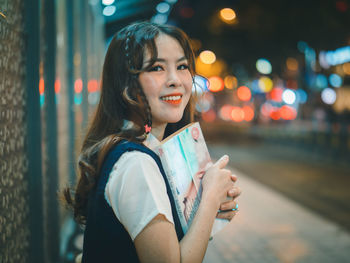 Portrait of smiling young woman standing in city at night