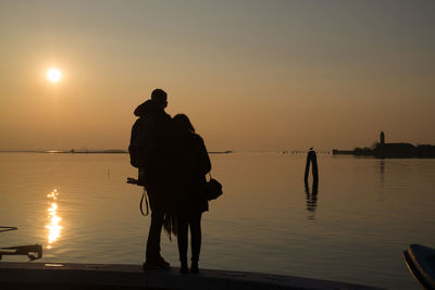 Silhouette people standing on beach against sky during sunset