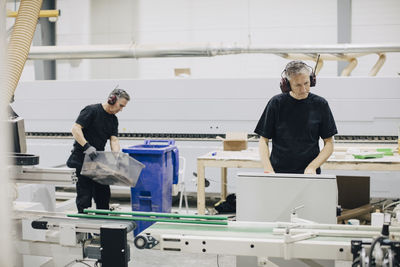 Mature man operating machine in industry while coworker working in background