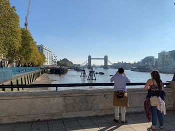 Rear view of people standing on bridge over river against sky