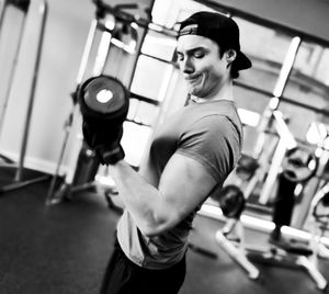 Side view of determined man lifting dumbbell at gym