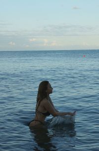 Side view of woman in sea against sky