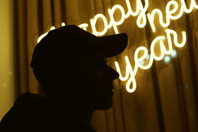 Close-up of silhouette man wearing cap against illuminated text