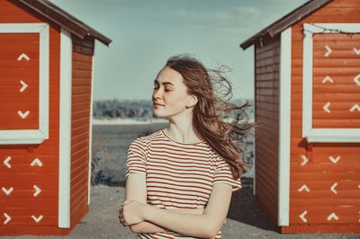 Young woman with arms crossed standing against beach houses